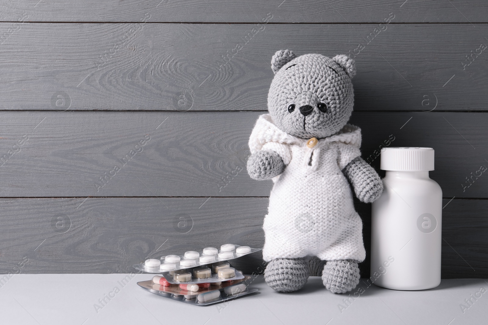 Photo of Toy bear with pills on light table near grey wooden wall, space for text