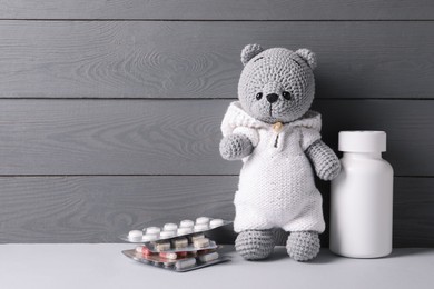Toy bear with pills on light table near grey wooden wall, space for text