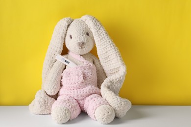 Toy bunny with thermometer on color background