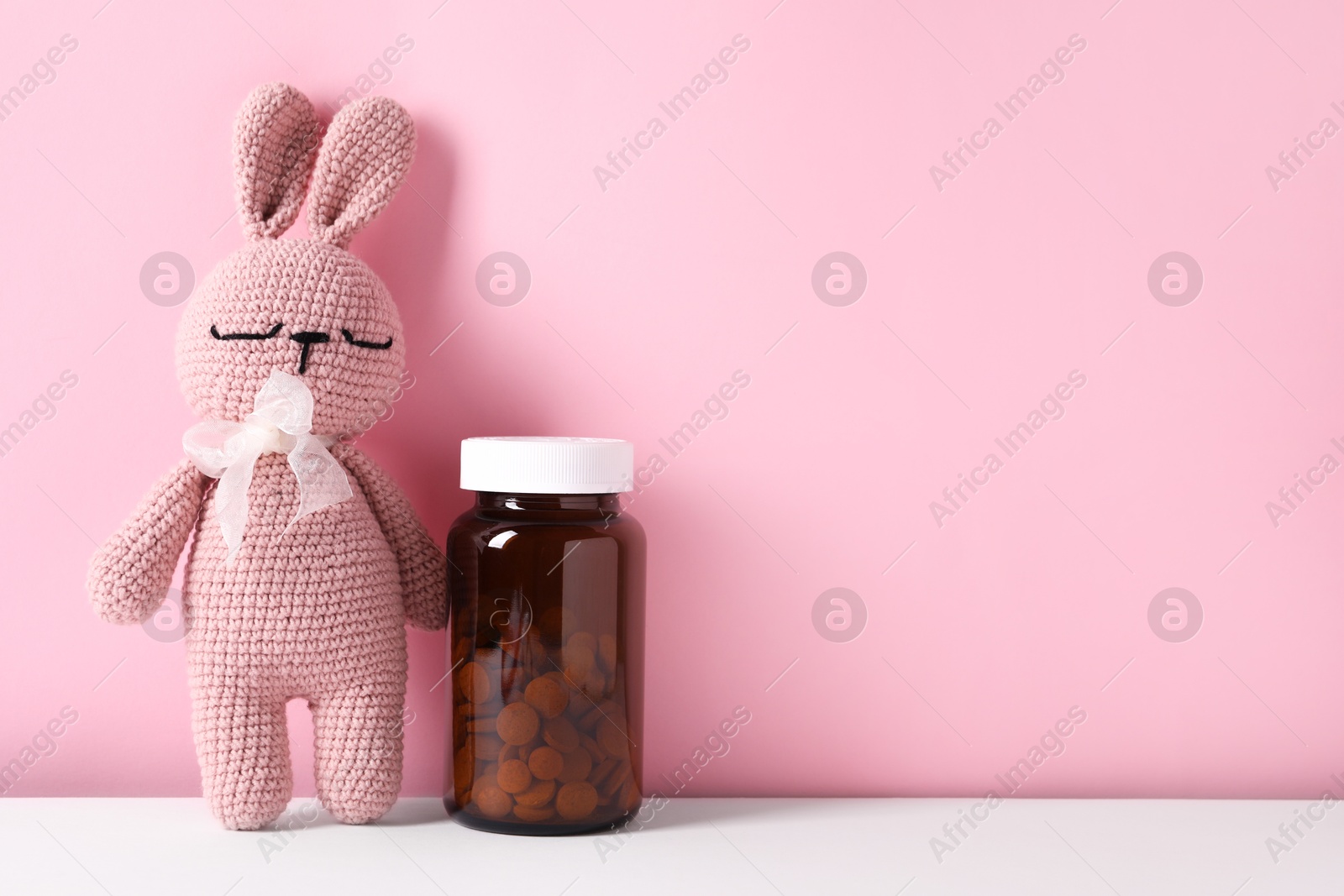 Photo of Toy bunny with bottle of pills on color background, space for text