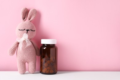 Photo of Toy bunny with bottle of pills on color background, space for text