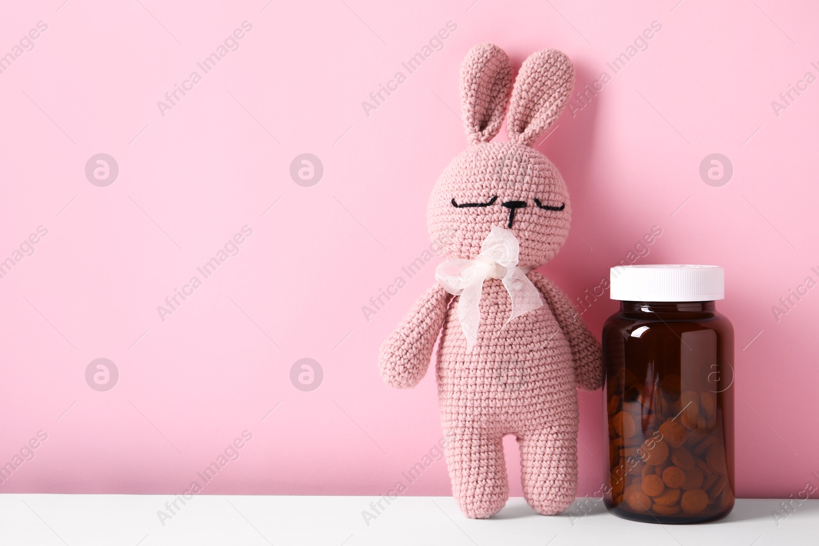 Photo of Toy bunny with bottle of pills on color background, space for text
