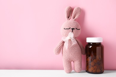 Toy bunny with bottle of pills on color background, space for text