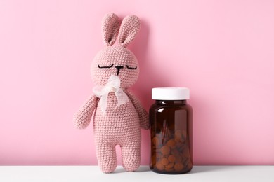 Toy bunny with bottle of pills on color background