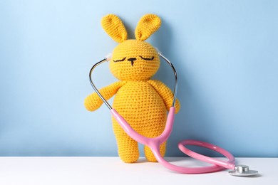 Toy bunny with stethoscope on color background