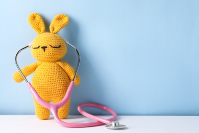 Toy bunny with stethoscope on color background, space for text