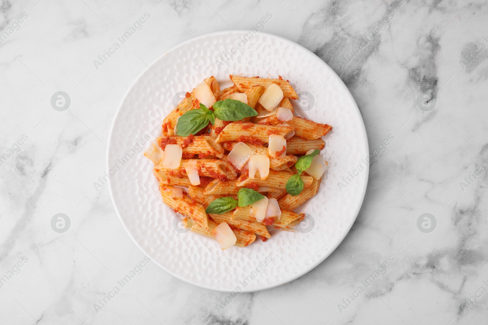 Photo of Tasty pasta with tomato sauce, cheese and basil on white marble table, top view