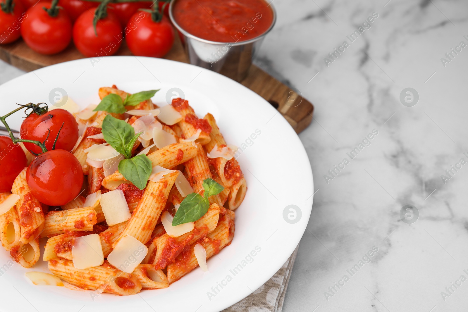 Photo of Tasty pasta with tomato sauce, cheese and basil on white marble table, space for text