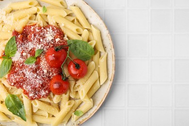 Tasty pasta with tomato sauce, cheese and basil on white tiled table, top view. Space for text