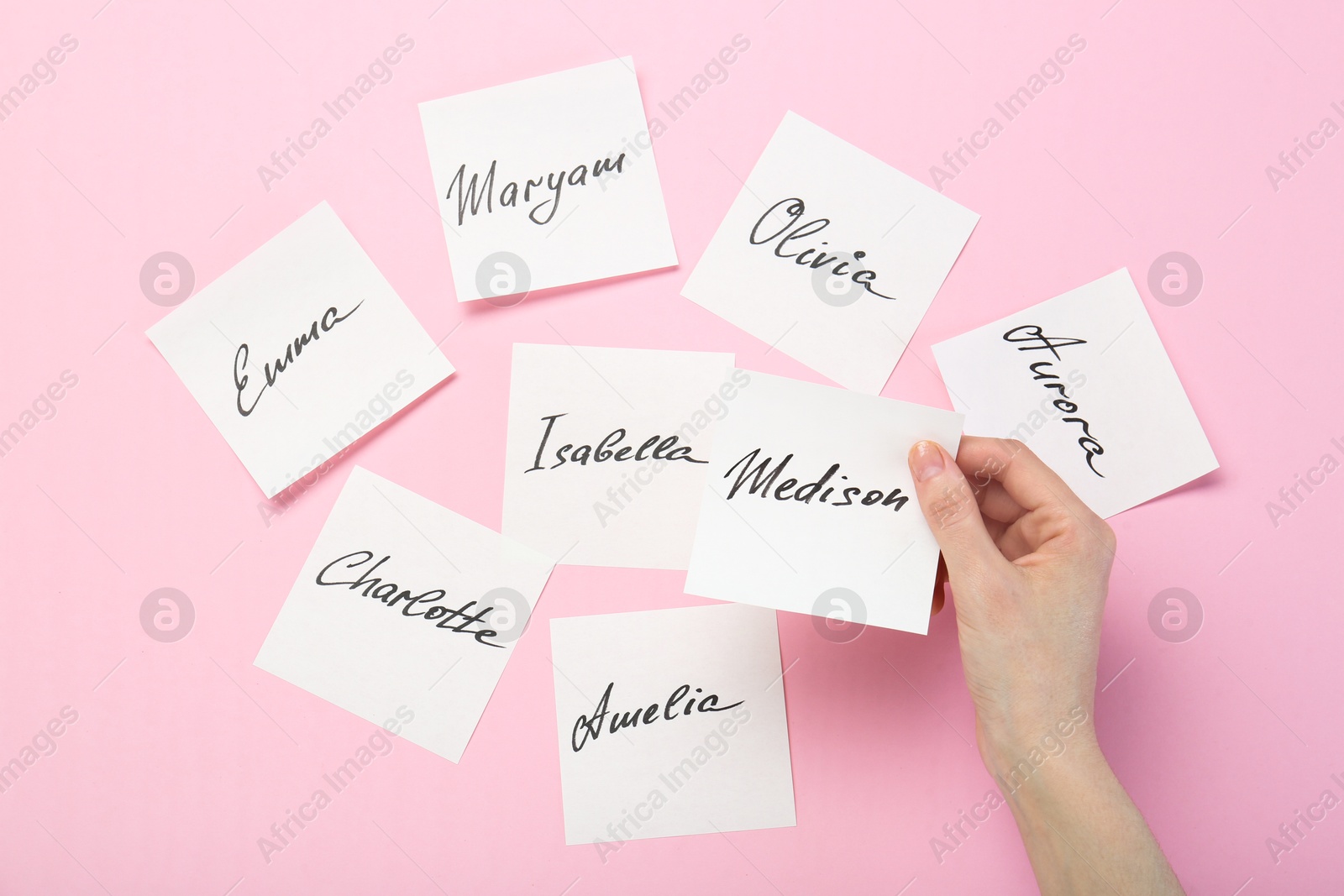 Photo of Woman holding paper stickers with name on pink background, top view. Choosing baby's name