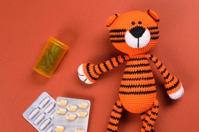 Photo of Toy tiger and pills on orange background, flat lay