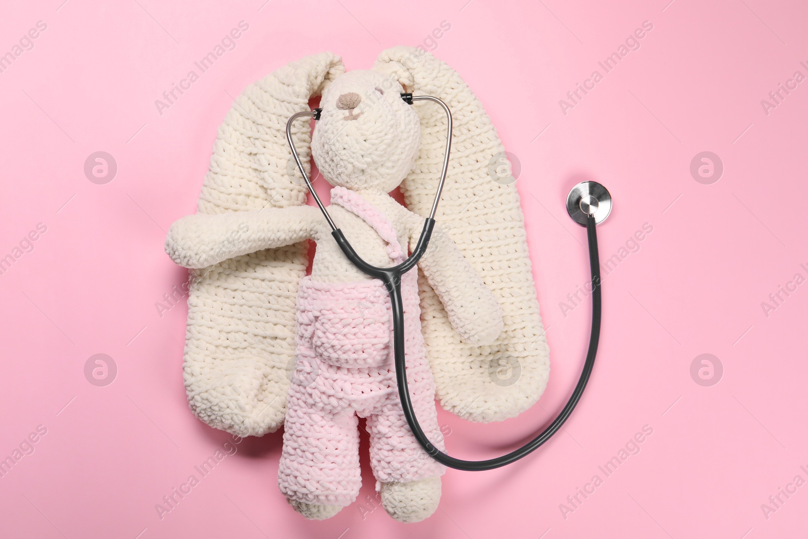 Photo of Toy bunny and stethoscope on pink background, top view