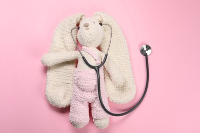 Photo of Toy bunny and stethoscope on pink background, top view