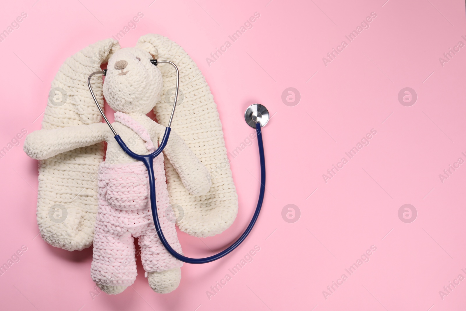 Photo of Toy bunny and stethoscope on pink background, top view. Space for text