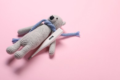 Photo of Toy bear and thermometer on pink background, space for text