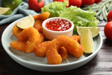 Delicious breaded fried shrimps, lime and sauce on wooden table, closeup