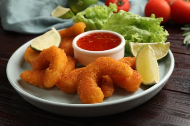 Delicious breaded fried shrimps, lime and sauce on wooden table, closeup