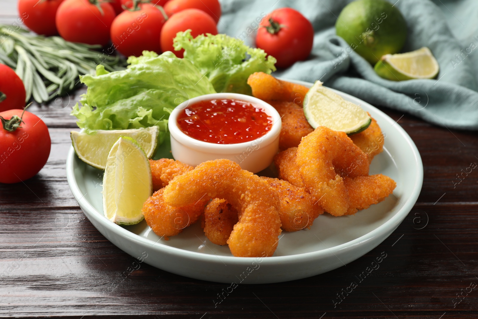 Photo of Delicious breaded fried shrimps, lime and sauce on wooden table