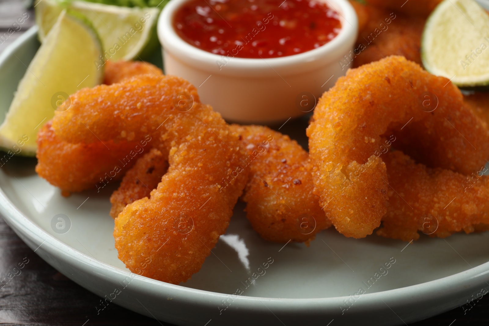 Photo of Delicious breaded fried shrimps, lime and sauce on table, closeup