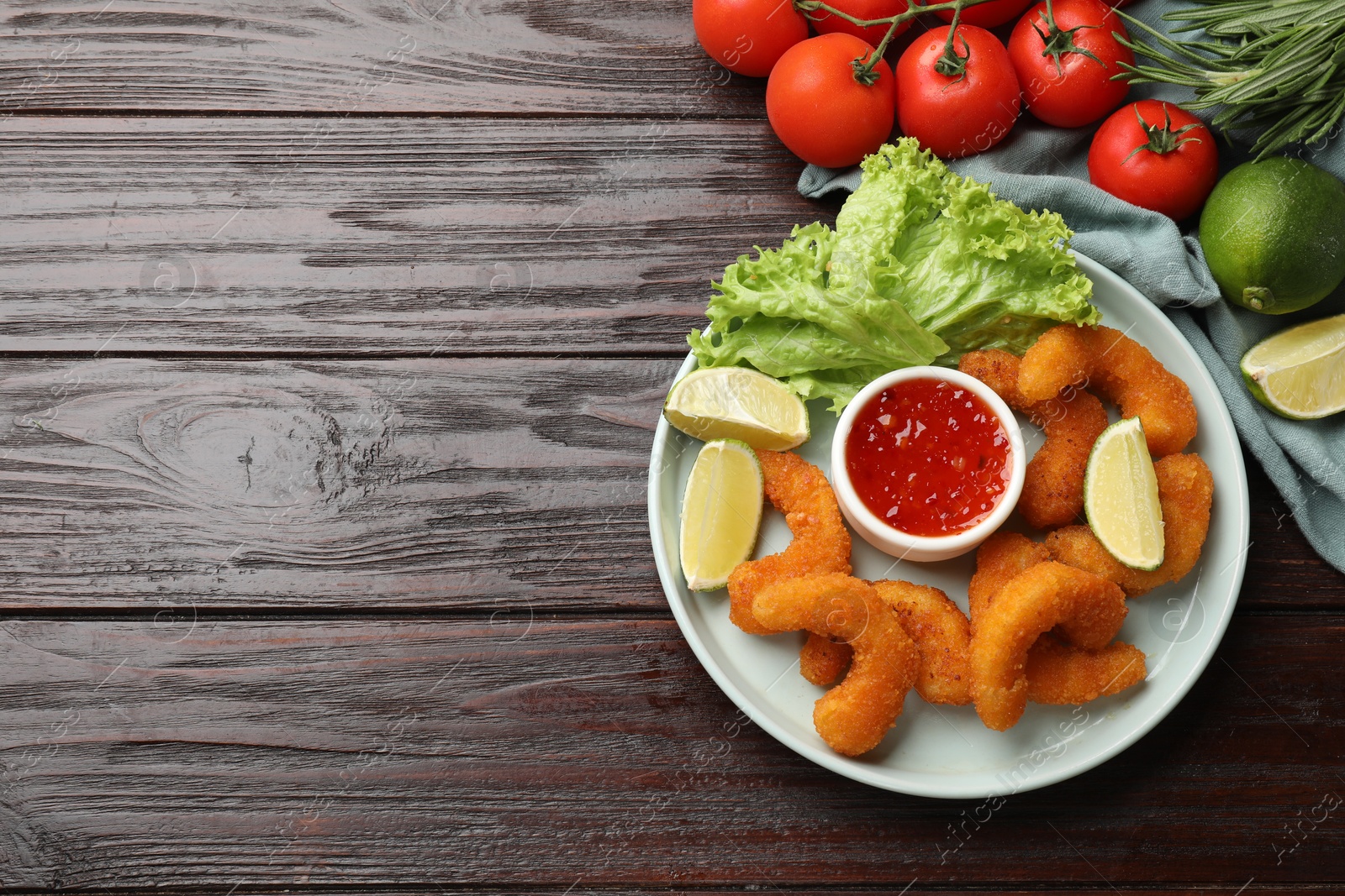 Photo of Delicious breaded fried shrimps served with lime and sauce on wooden table, top view. Space for text