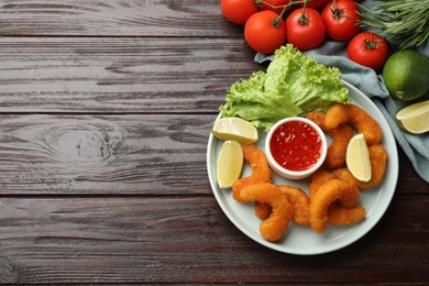 Delicious breaded fried shrimps served with lime and sauce on wooden table, top view. Space for text