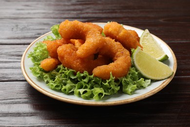 Photo of Delicious breaded fried shrimps, lime and lettuce on wooden table