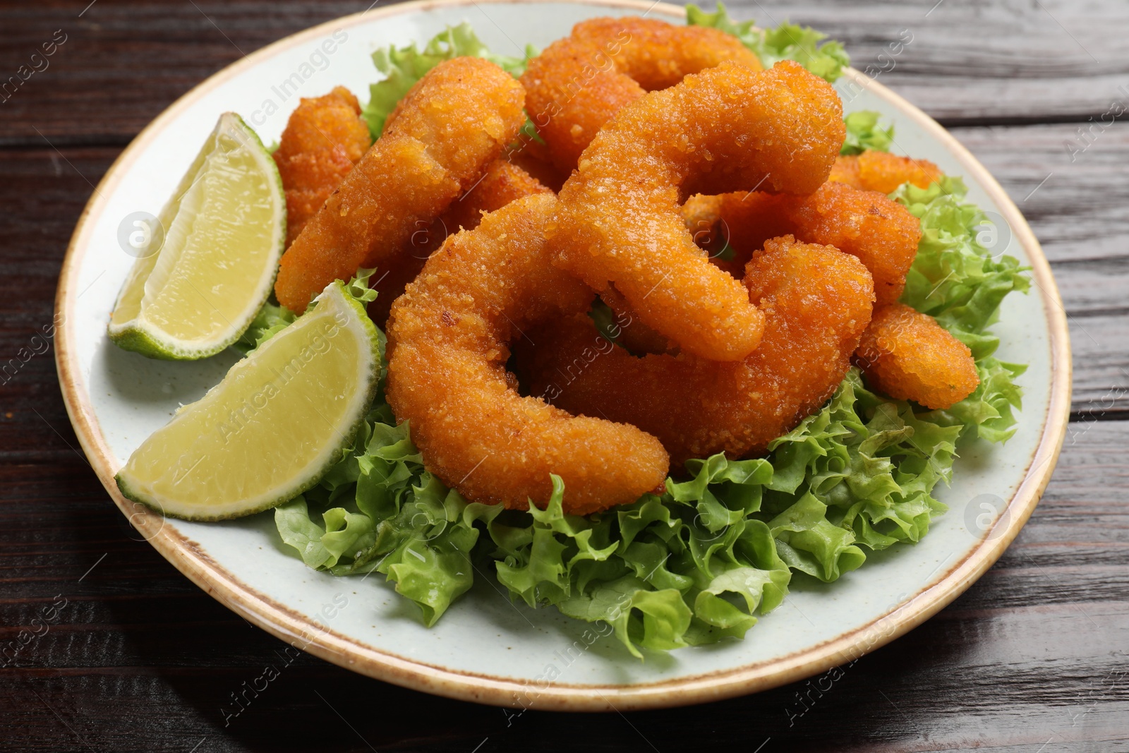 Photo of Delicious breaded fried shrimps, lime and lettuce on wooden table