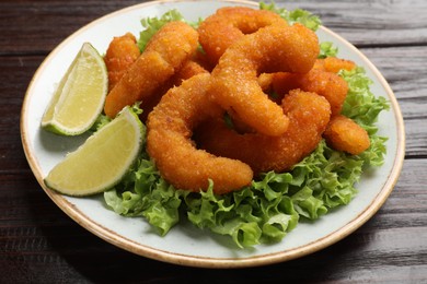 Photo of Delicious breaded fried shrimps, lime and lettuce on wooden table