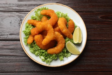 Photo of Delicious breaded fried shrimps, lime and lettuce on wooden table, top view