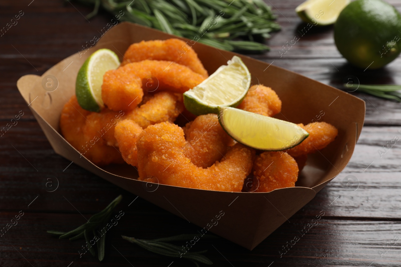 Photo of Delicious breaded fried shrimps, lime and rosemary on wooden table