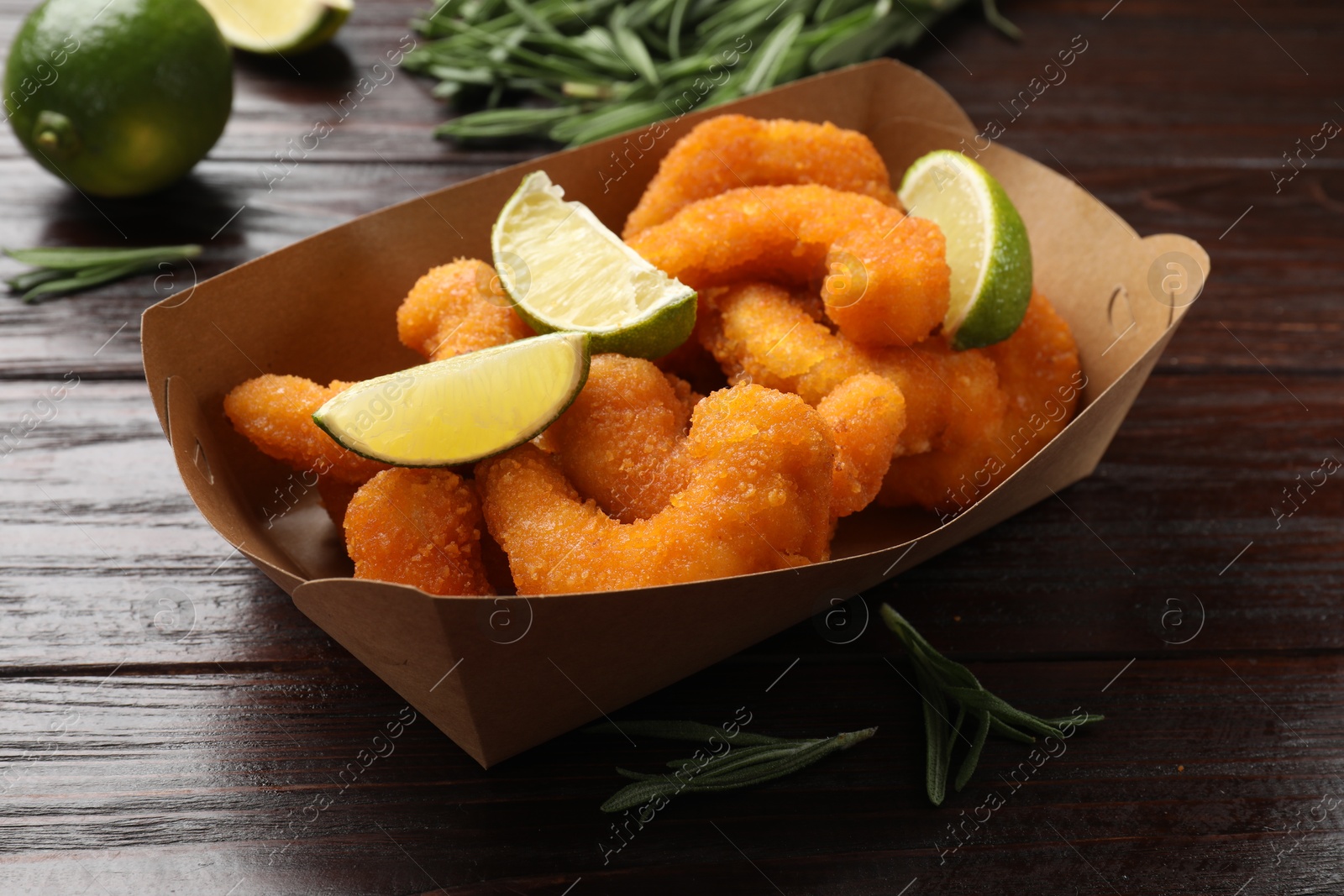 Photo of Delicious breaded fried shrimps, lime and rosemary on wooden table