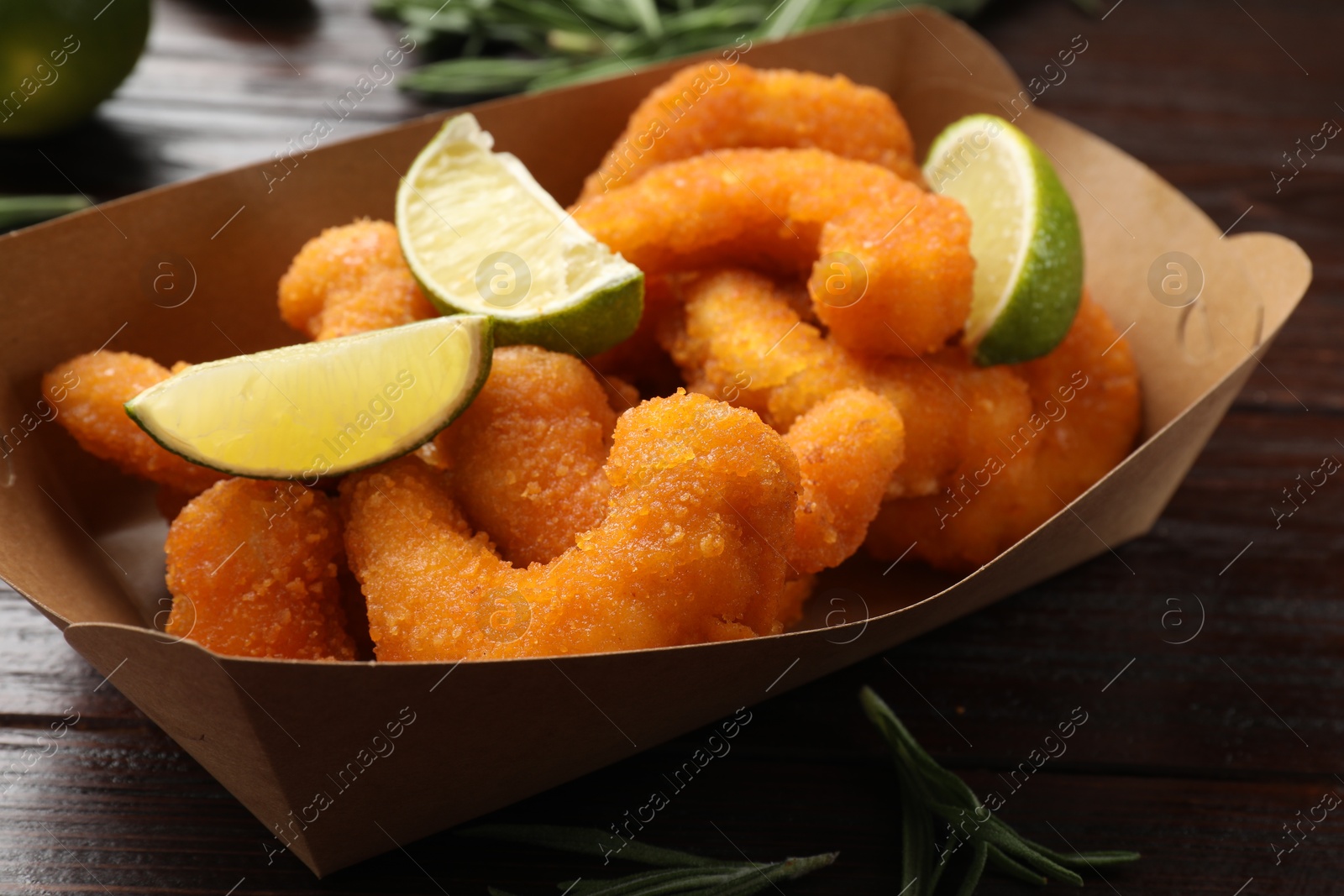 Photo of Delicious breaded fried shrimps, lime and rosemary on wooden table, closeup