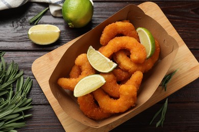 Delicious breaded fried shrimps, lime and rosemary on wooden table, top view