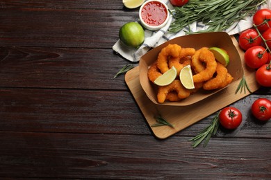 Photo of Delicious breaded fried shrimps served with lime and sauce on wooden table, top view. Space for text