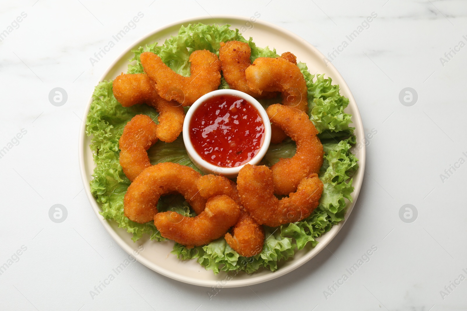 Photo of Delicious breaded fried shrimps, sauce and lettuce on white marble table, top view