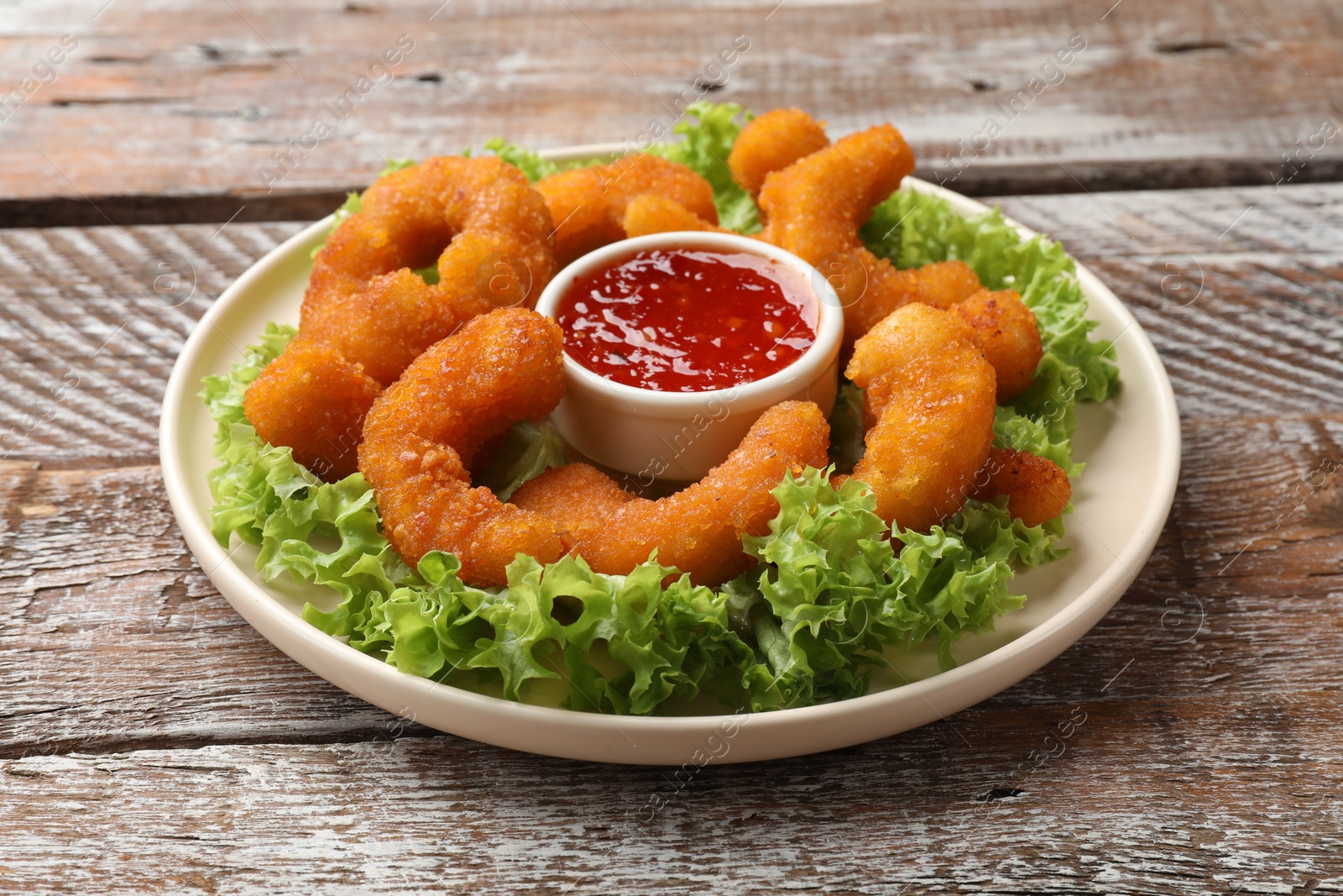 Photo of Delicious breaded fried shrimps, sauce and lettuce on wooden table