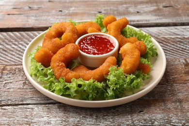 Photo of Delicious breaded fried shrimps, sauce and lettuce on wooden table