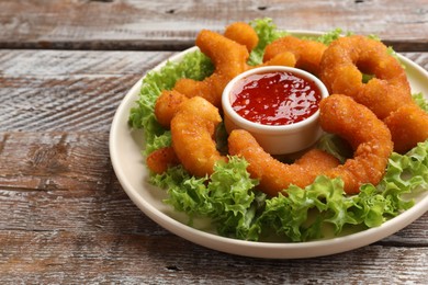 Photo of Delicious breaded fried shrimps, sauce and lettuce on wooden table