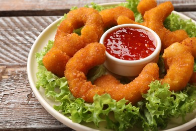 Photo of Delicious breaded fried shrimps, sauce and lettuce on wooden table, closeup