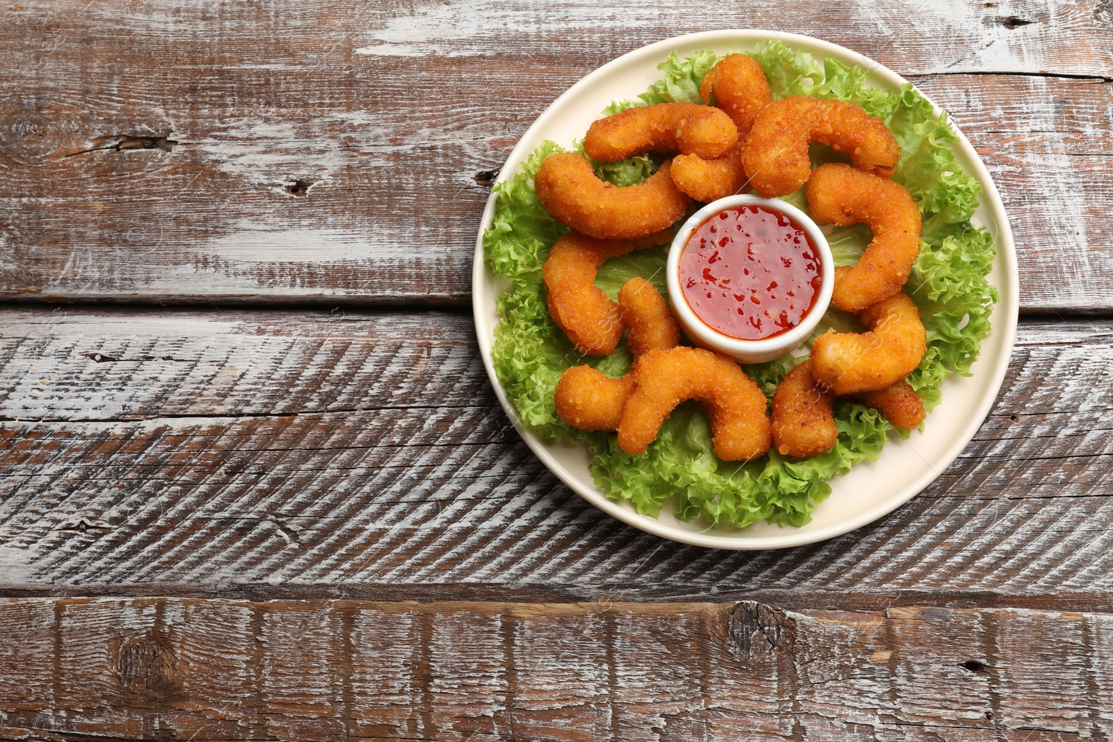 Photo of Delicious breaded fried shrimps, sauce and lettuce on wooden table, top view. Space for text