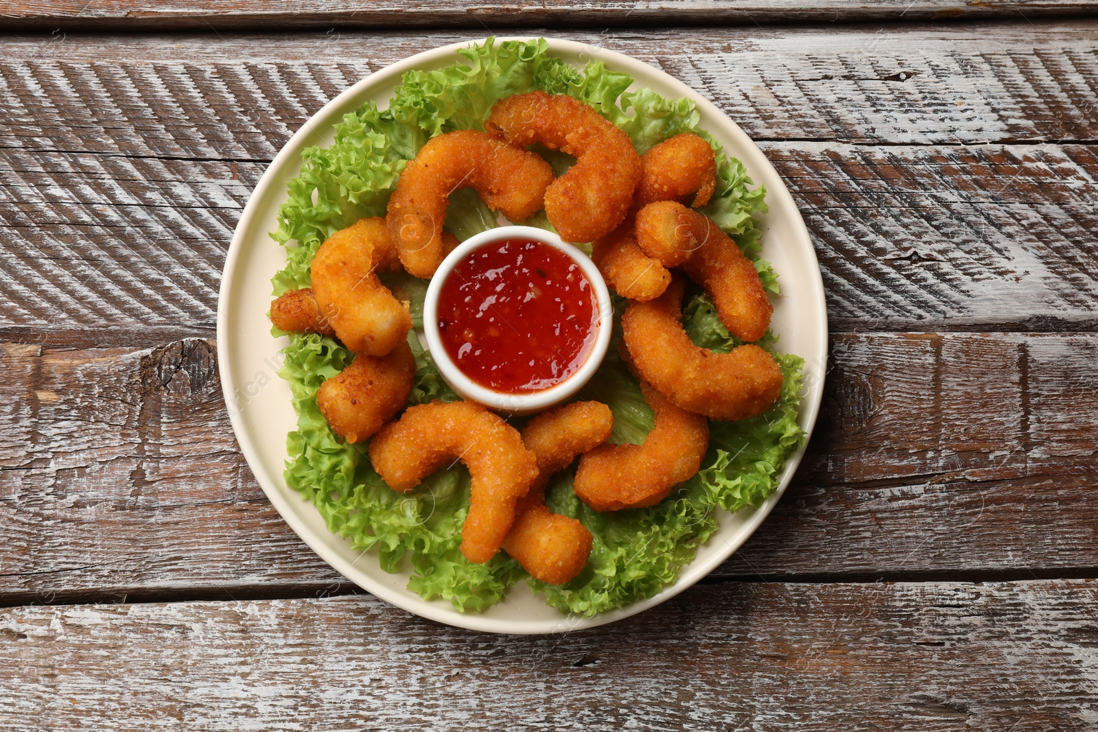 Photo of Delicious breaded fried shrimps, sauce and lettuce on wooden table, top view