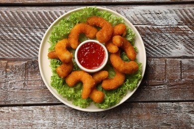 Delicious breaded fried shrimps, sauce and lettuce on wooden table, top view