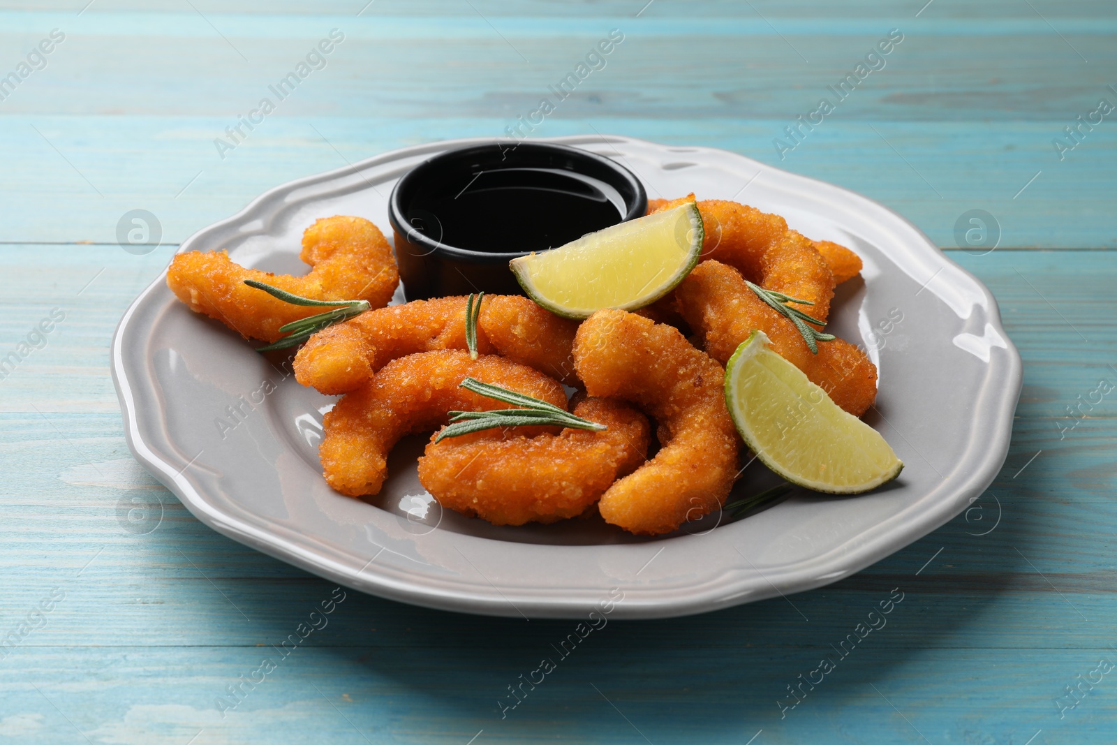 Photo of Delicious breaded fried shrimps, lime, rosemary and sauce on light blue wooden table