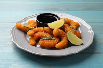 Photo of Delicious breaded fried shrimps, lime, rosemary and sauce on light blue wooden table