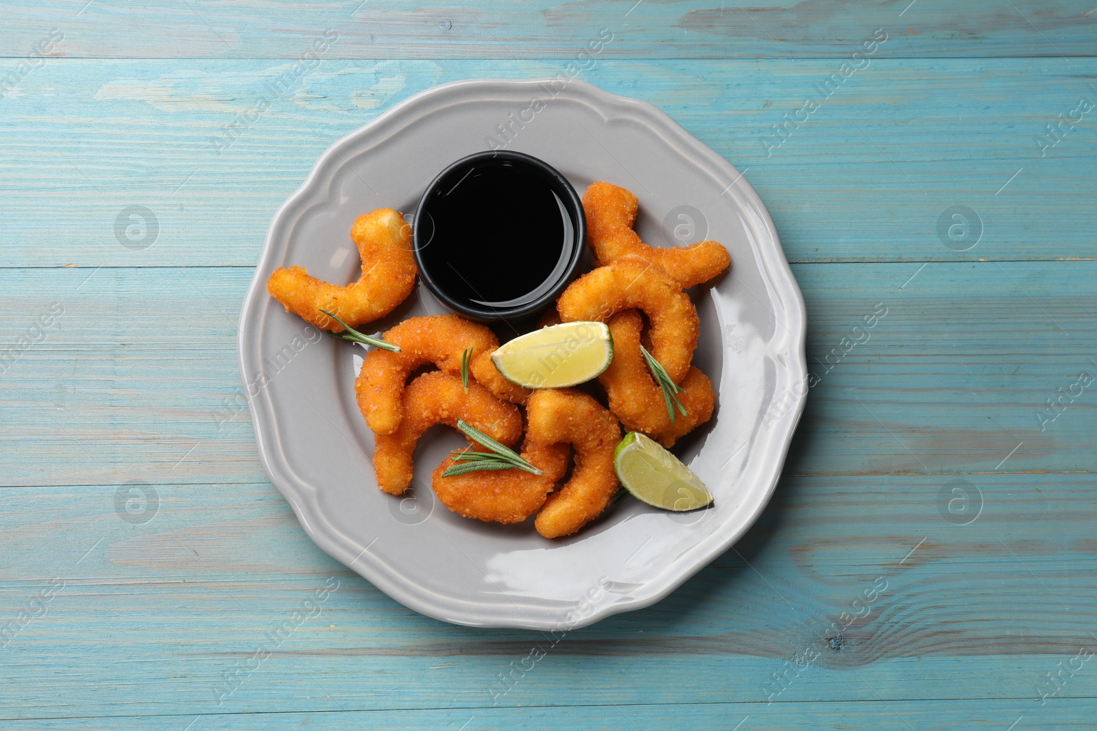 Photo of Delicious breaded fried shrimps, lime, rosemary and sauce on light blue wooden table, top view