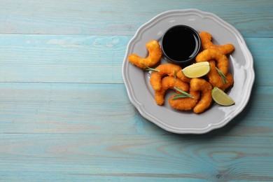 Photo of Delicious breaded fried shrimps, lime, rosemary and sauce on light blue wooden table, top view. Space for text