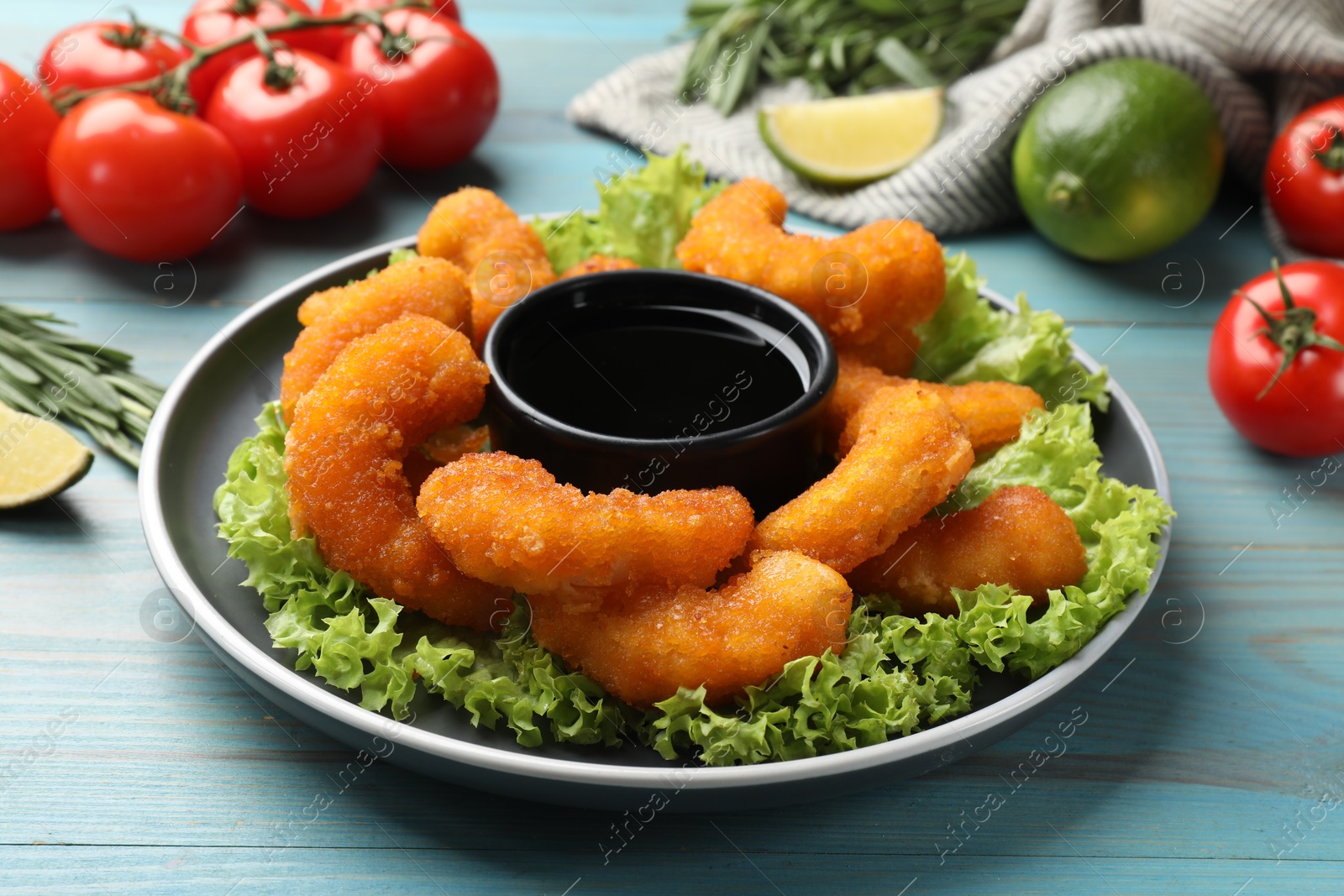 Photo of Delicious breaded fried shrimps served with sauce on light blue wooden table