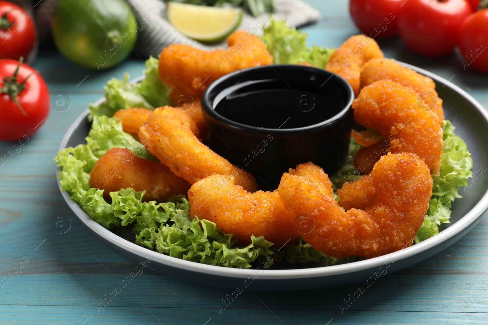 Photo of Delicious breaded fried shrimps served with sauce on light blue wooden table, closeup