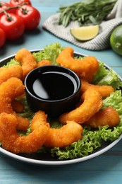 Photo of Delicious breaded fried shrimps served with sauce on light blue wooden table, closeup