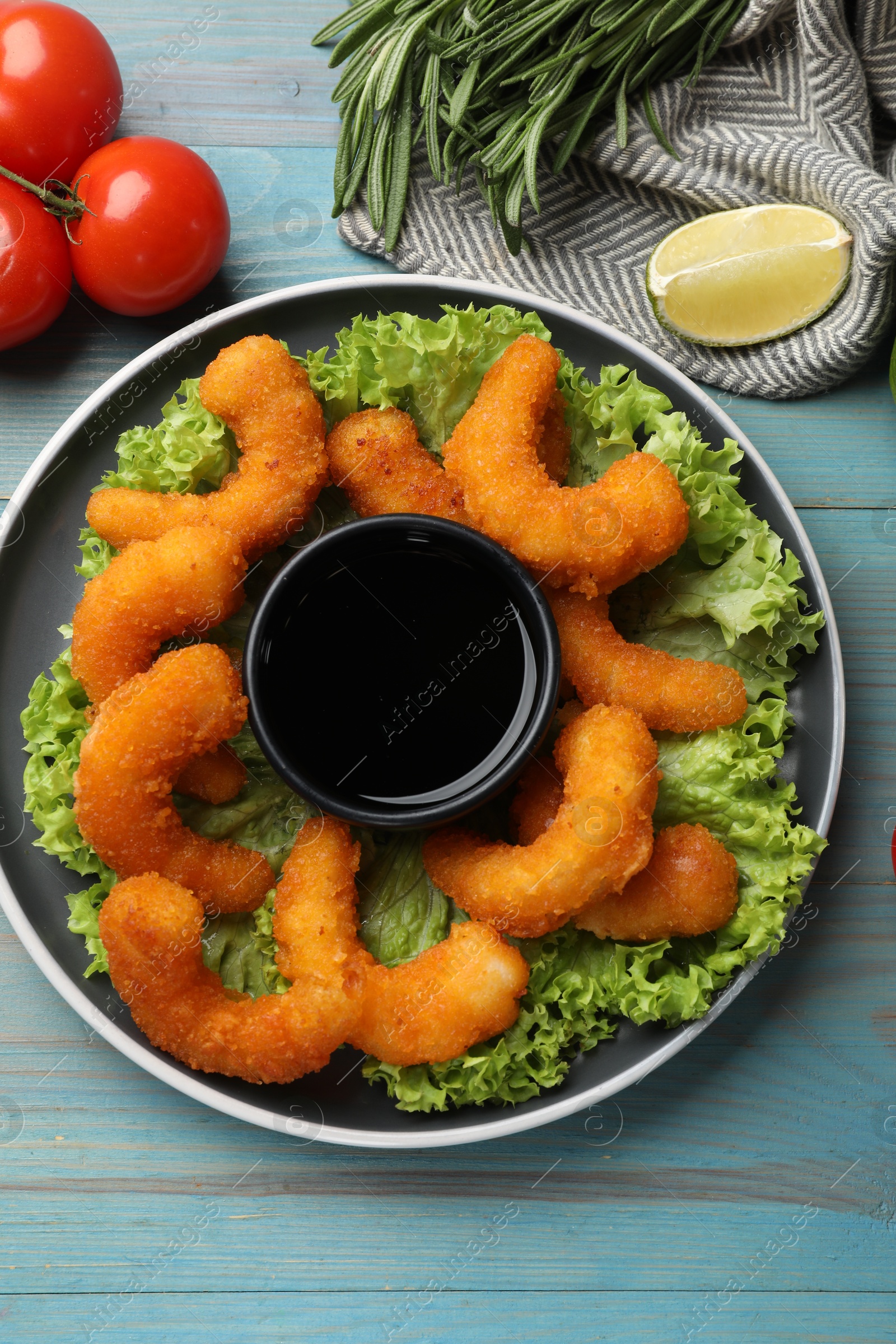 Photo of Delicious breaded fried shrimps served with sauce on light blue wooden table, top view